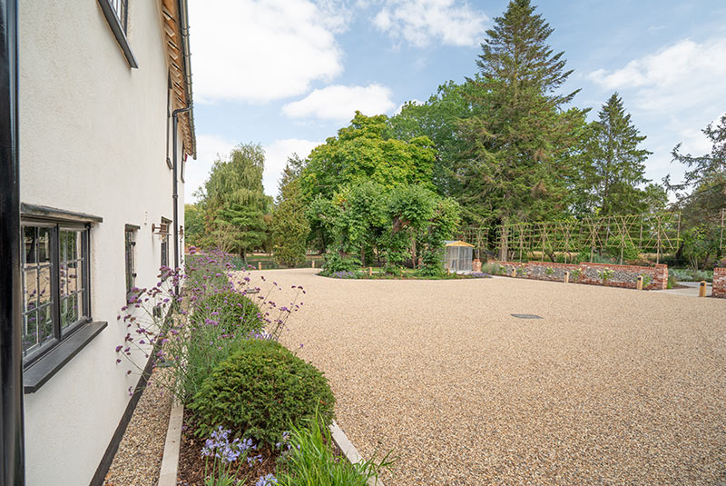 A landscaped garden at Porters Hall featuring a large stone patio, outdoor dining furniture, and a barbecue area for guest use.