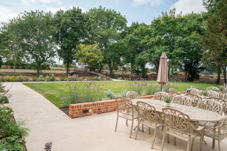 A landscaped garden at Porters Hall featuring a large stone patio, outdoor dining furniture, and a barbecue area for guest use.