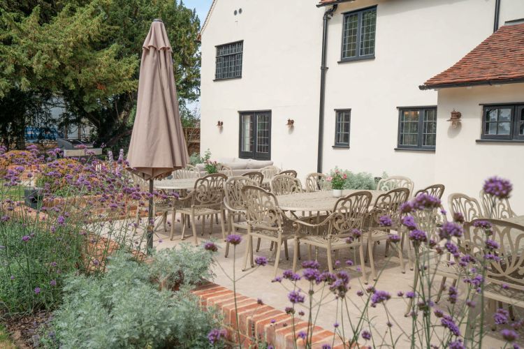 A landscaped garden at Porters Hall featuring a large stone patio, outdoor dining furniture, and a barbecue area for guest use.
