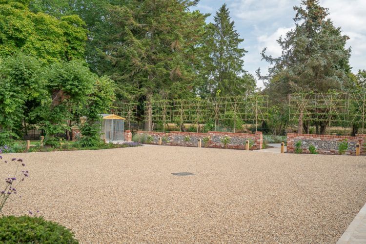 A landscaped garden at Porters Hall featuring a large stone patio, outdoor dining furniture, and a barbecue area for guest use.