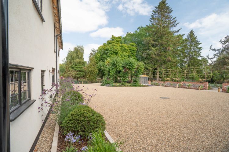 A landscaped garden at Porters Hall featuring a large stone patio, outdoor dining furniture, and a barbecue area for guest use.