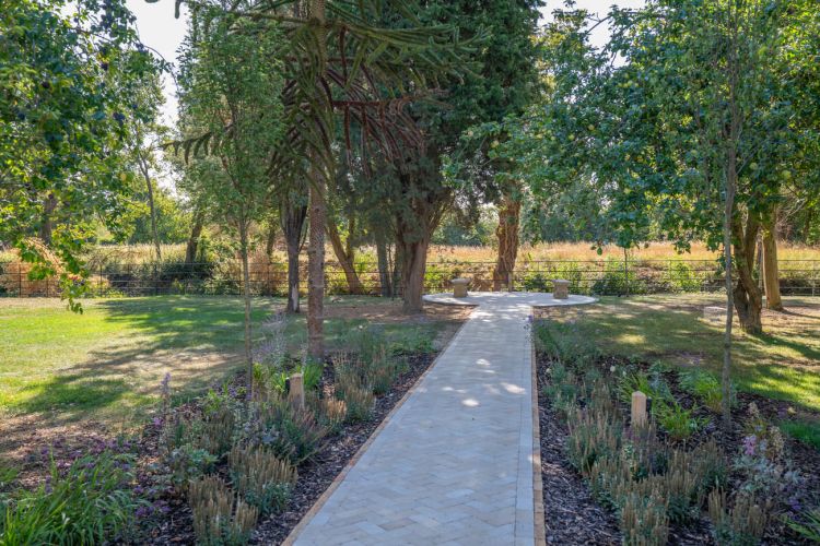 A landscaped garden at Porters Hall featuring a large stone patio, outdoor dining furniture, and a barbecue area for guest use.